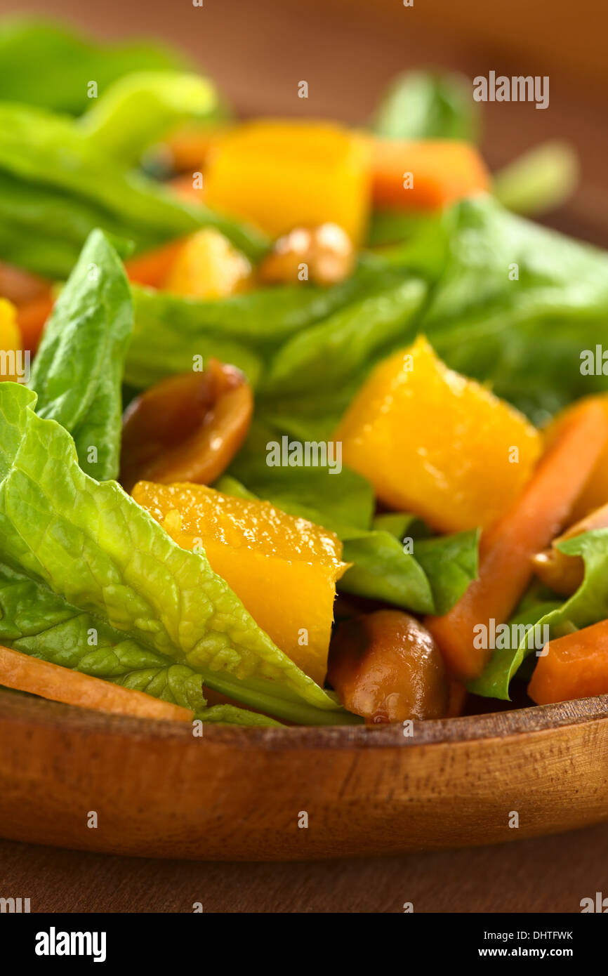 Spinaci freschi, mango e insalata di carote con arachidi sul piatto di legno (messa a fuoco selettiva, messa a fuoco sulla parte anteriore dell'insalata) Foto Stock