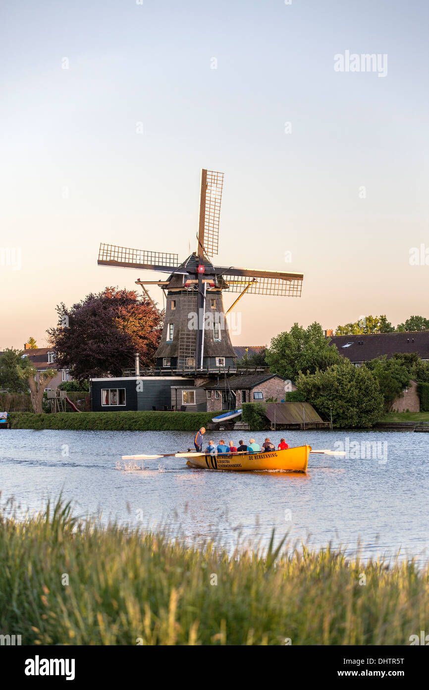 I Paesi Bassi, Weesp, gente che canottaggio sul fiume Vecht. Mulino a vento per macinare la farina. Foto Stock