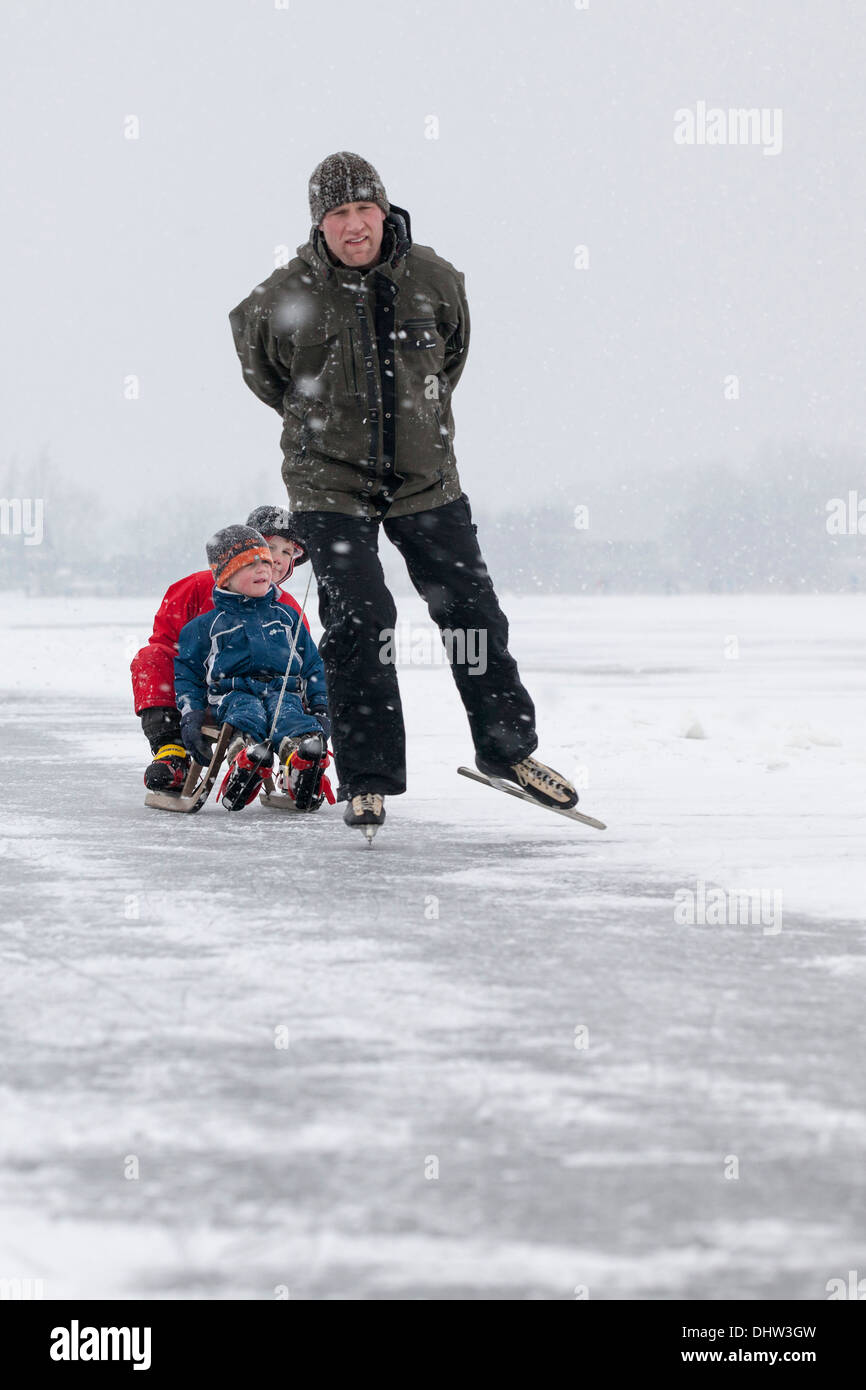 Paesi Bassi, Loosdrecht, laghi chiamato Loosdrechtse Plassen. L'inverno. Padre pattinaggio sul ghiaccio con figli su slitta Foto Stock