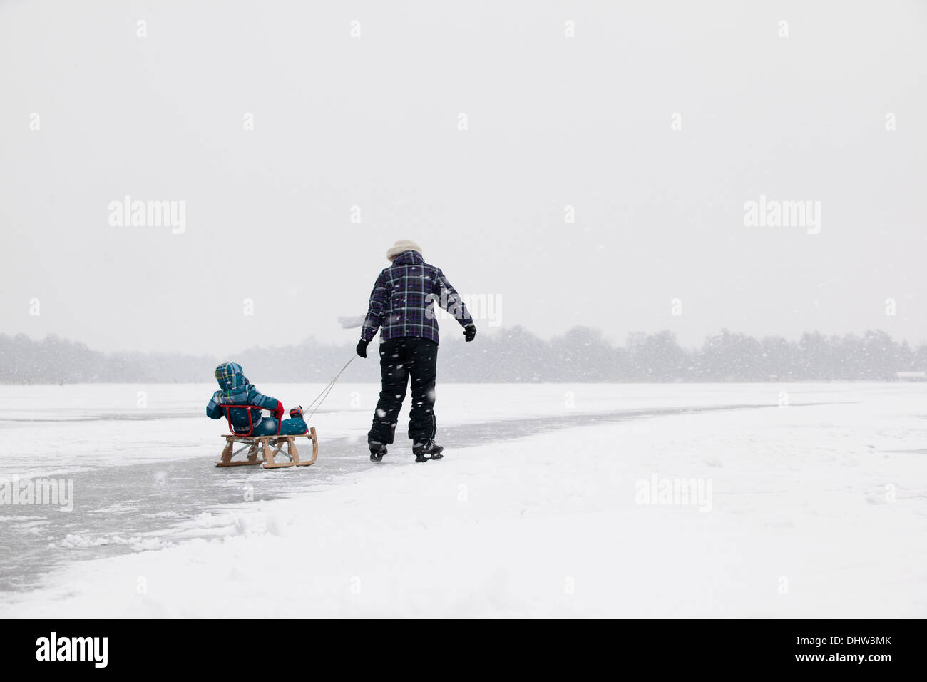 Paesi Bassi, Loosdrecht, laghi chiamato Loosdrechtse Plassen. L'inverno. Madre pattinaggio sul ghiaccio con bambino sulla slitta Foto Stock