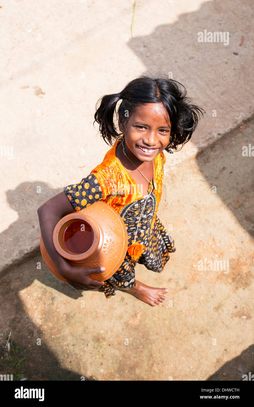 Ragazza indiana che porta un vaso in materia plastica con acqua da un tubo montante in un territorio rurale villaggio indiano street. Andhra Pradesh, India Foto Stock