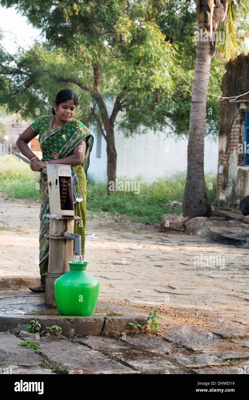 Donna indiana di riempimento acqua in plastica vaso da un villaggio rurale la pompa a mano. Andhra Pradesh, India Foto Stock