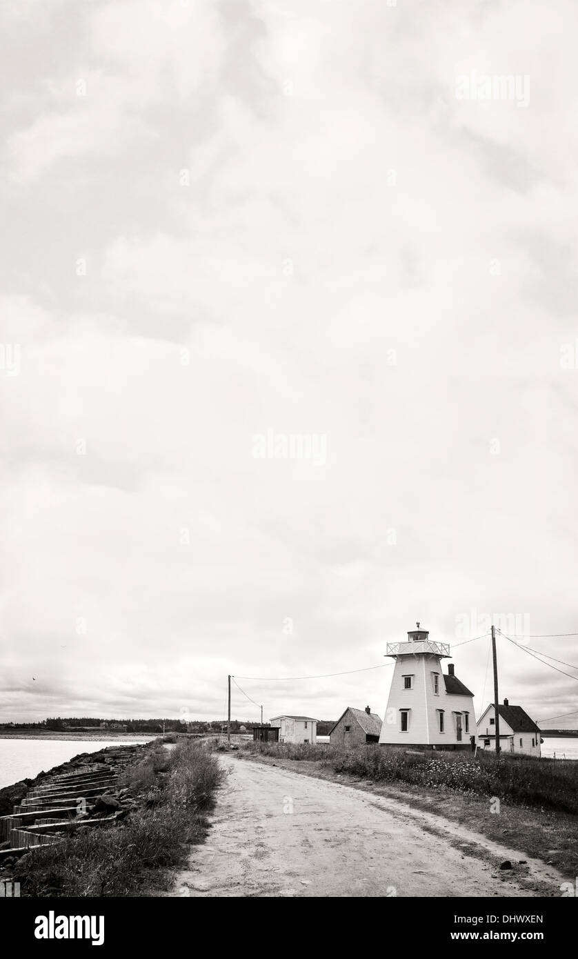 Una fotografia in bianco e nero di una remota città costiera con il faro, cottage e un burrascoso cielo minaccioso. Foto Stock