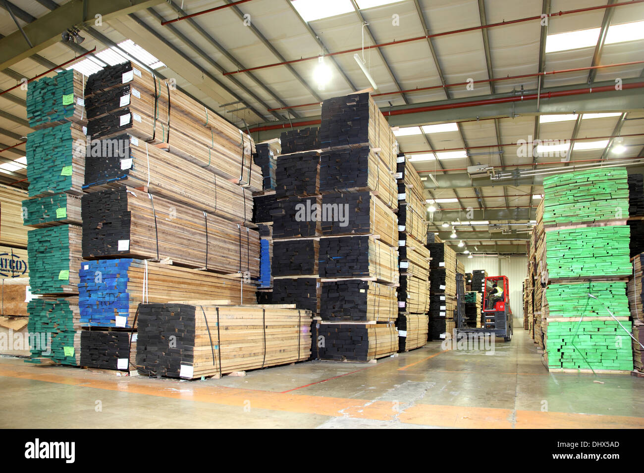 Un carrello elevatore a forca manoeveres tra grandi pile di legname segato in un moderno magazzino di stoccaggio Foto Stock