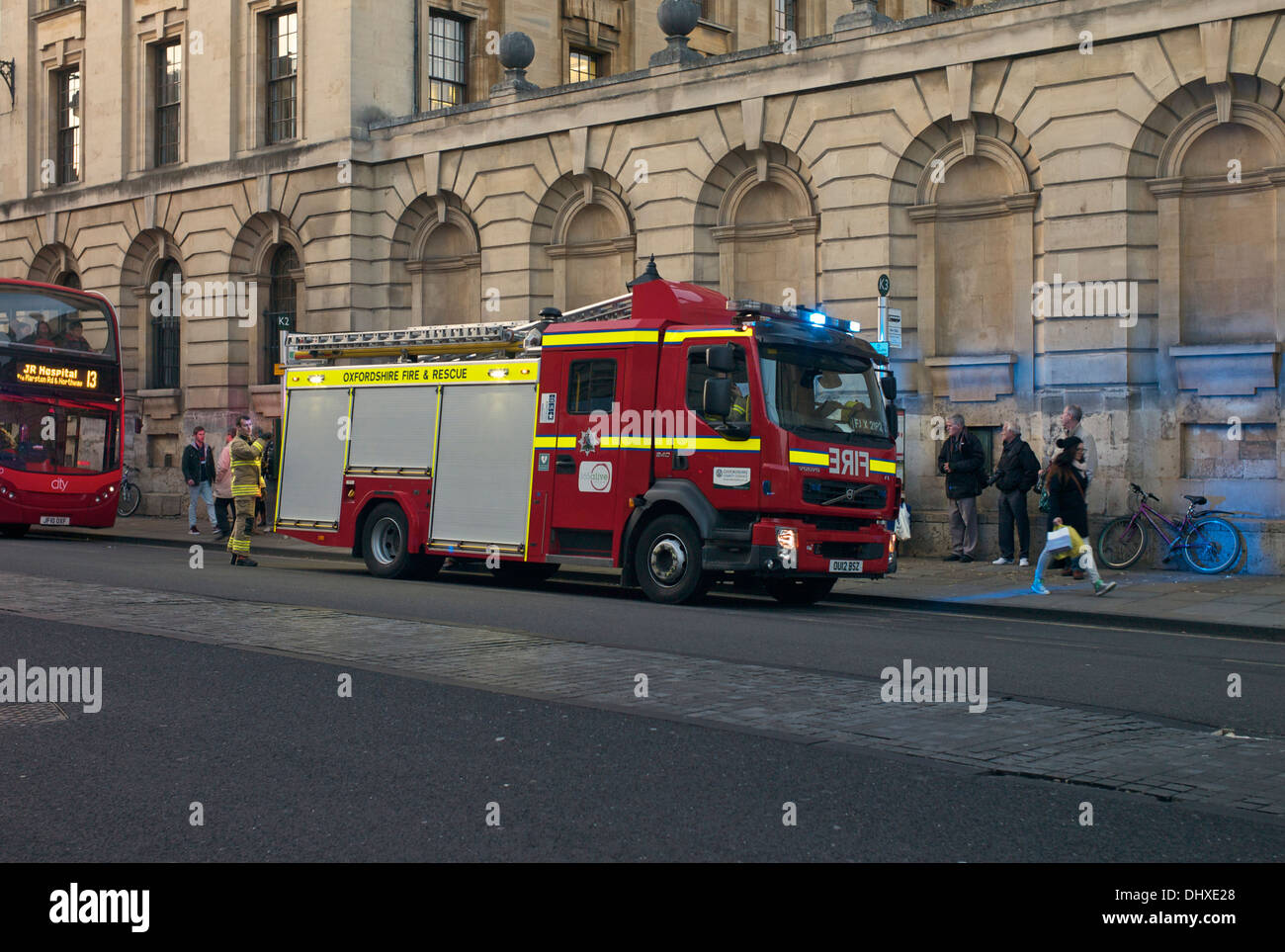 Vigili del fuoco da Oxfordshire Fire & Rescue Service frequentare un incidente sulla strada alta. Pedoni e passeggeri di un autobus watch Foto Stock