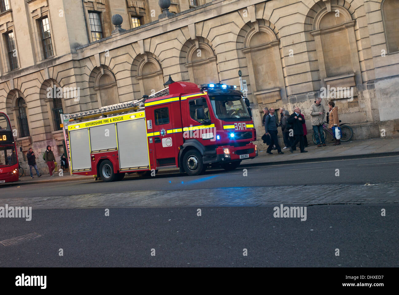 Vigili del fuoco da Oxfordshire Fire & Rescue Service frequentare un incidente sulla strada alta. Pedoni e passeggeri di un autobus watch Foto Stock