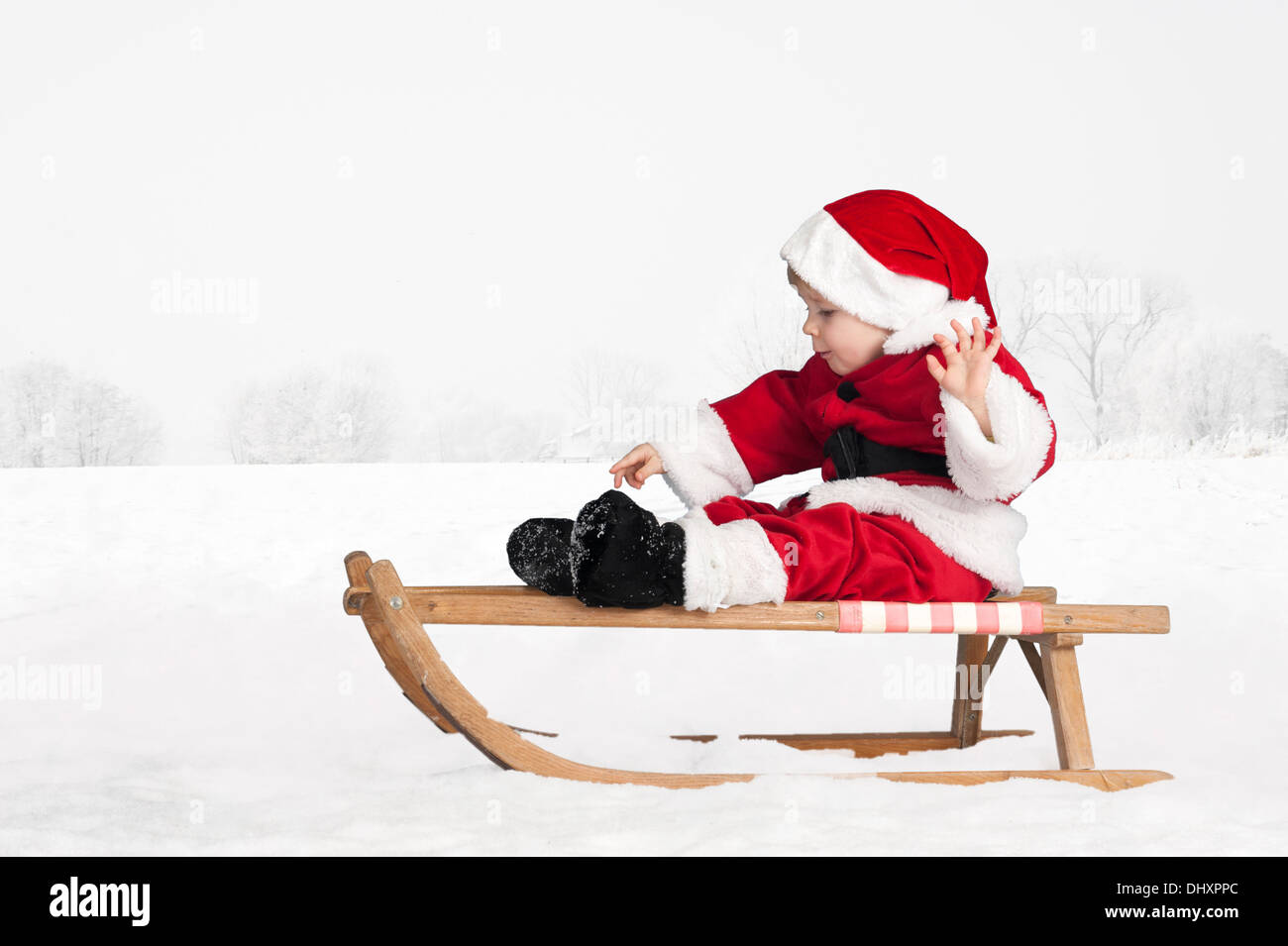 Piccolo bimbo in santa claus vestito su una slitta all'aperto nella neve Foto Stock