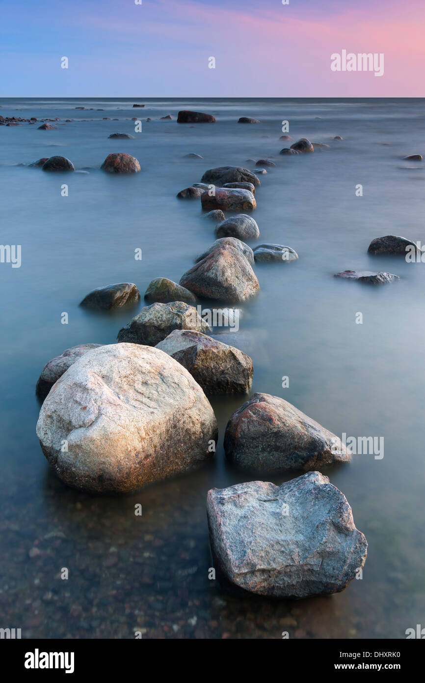 Riga su grosse pietre o roccia s in mare al tramonto Foto Stock