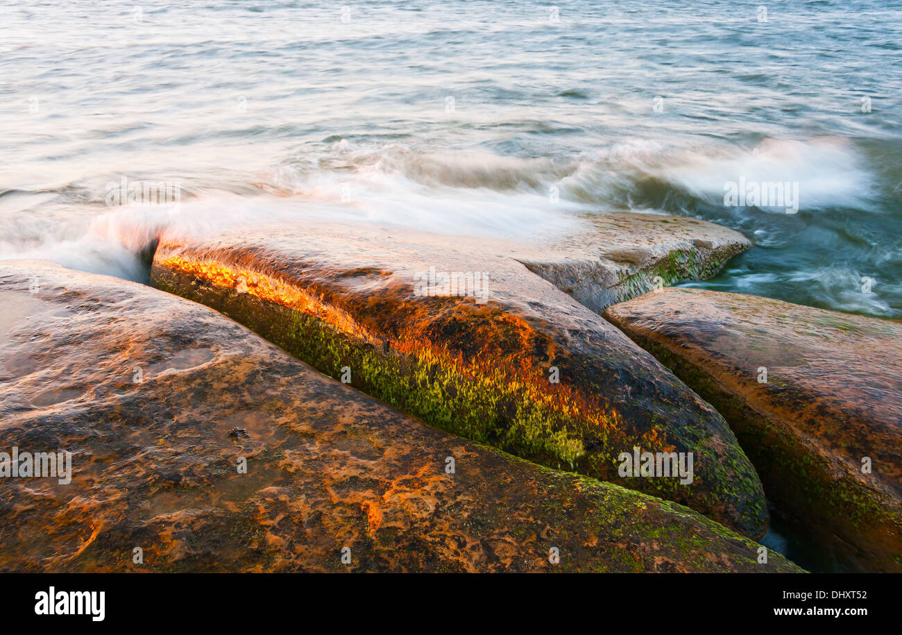 Onde di acqua su grandi rocce brunastro in mare Foto Stock
