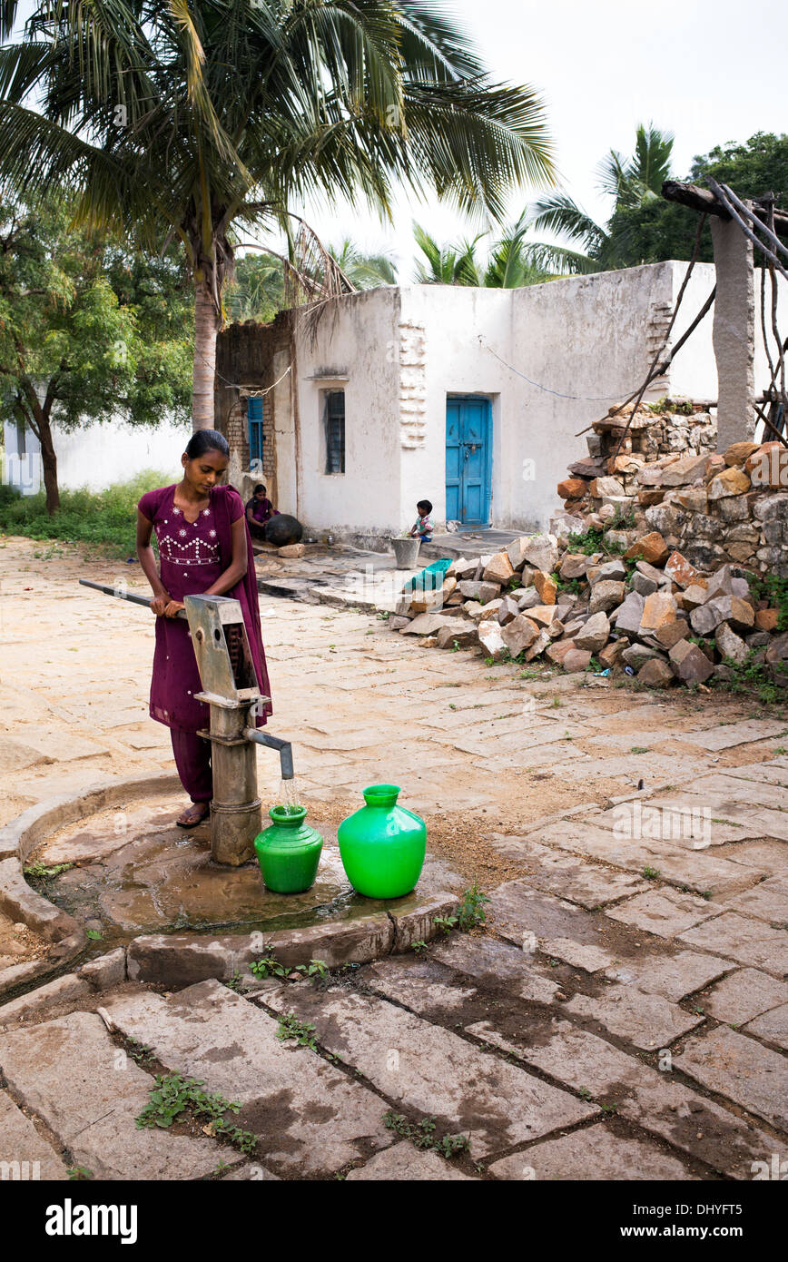 Indian ragazza adolescente il pompaggio di acqua da una pompa a mano in una pentola in un territorio rurale villaggio indiano. Andhra Pradesh, India. Foto Stock