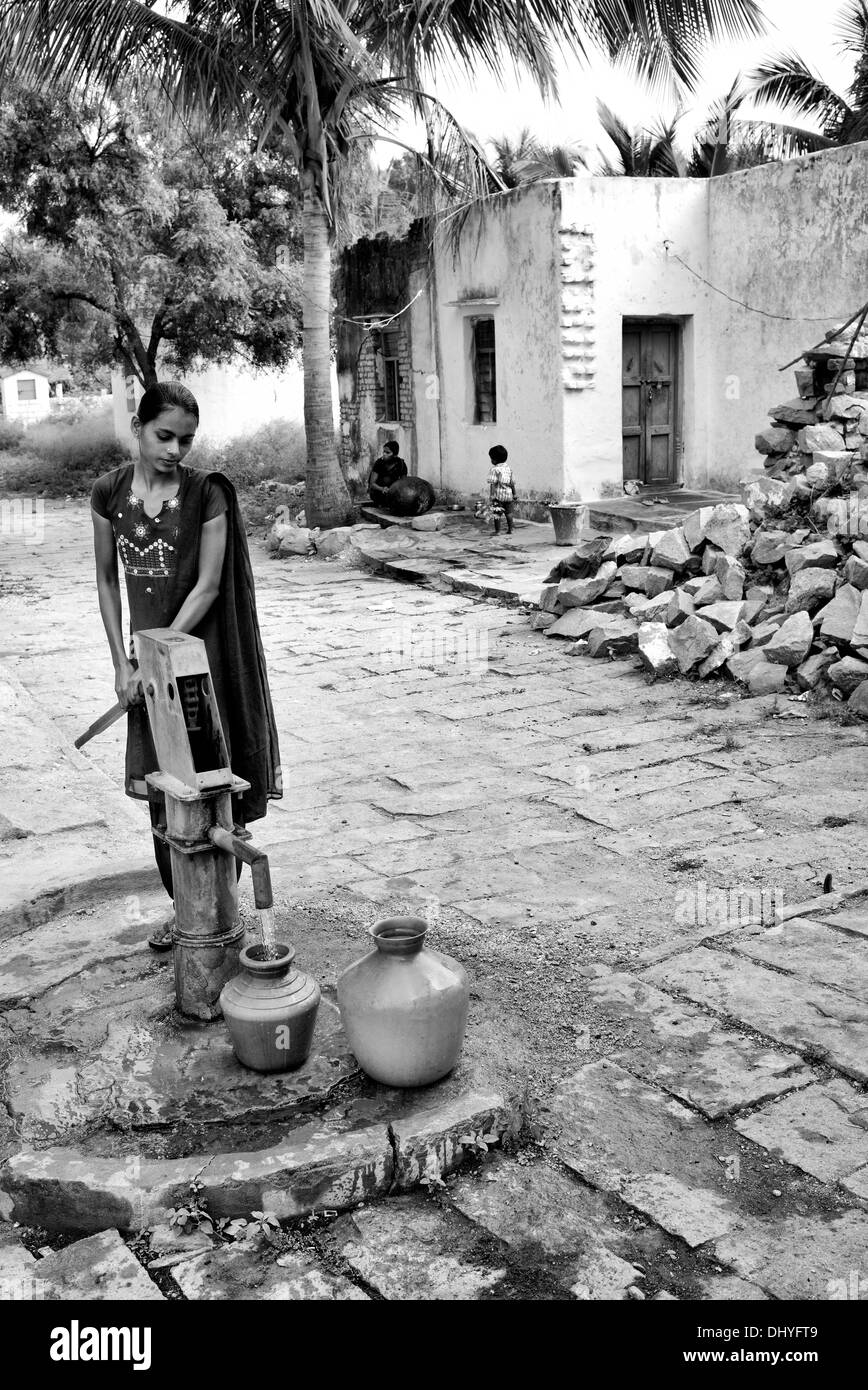 Indian ragazza adolescente il pompaggio di acqua da una pompa a mano in una pentola in un territorio rurale villaggio indiano. Andhra Pradesh, India. Monocromatico Foto Stock