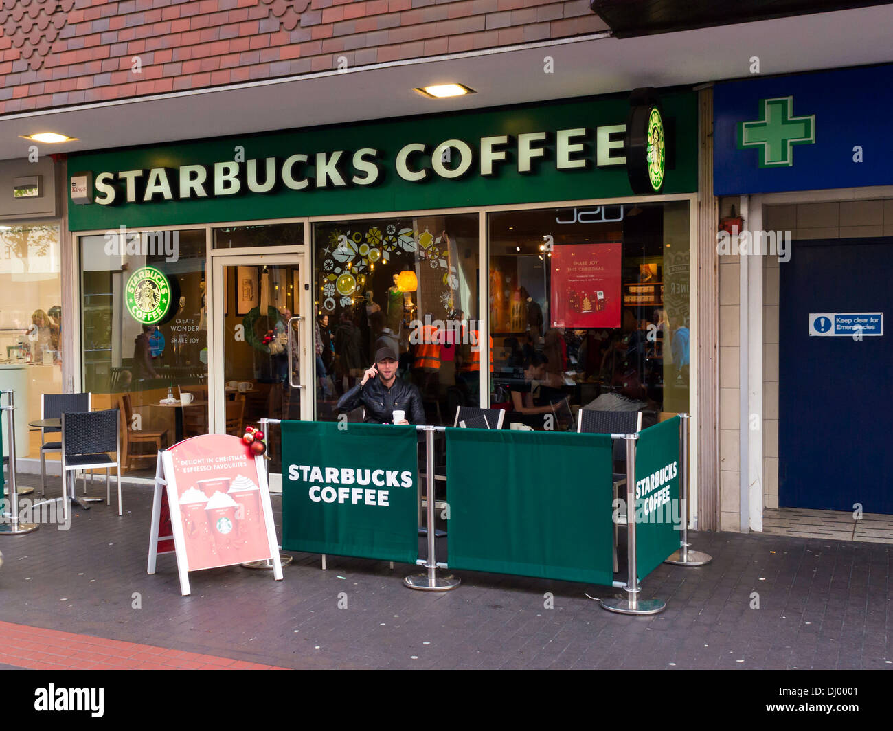 Uomo in posti a sedere fuori di Starbucks Coffee Shop parlando a un telefono cellulare Foto Stock