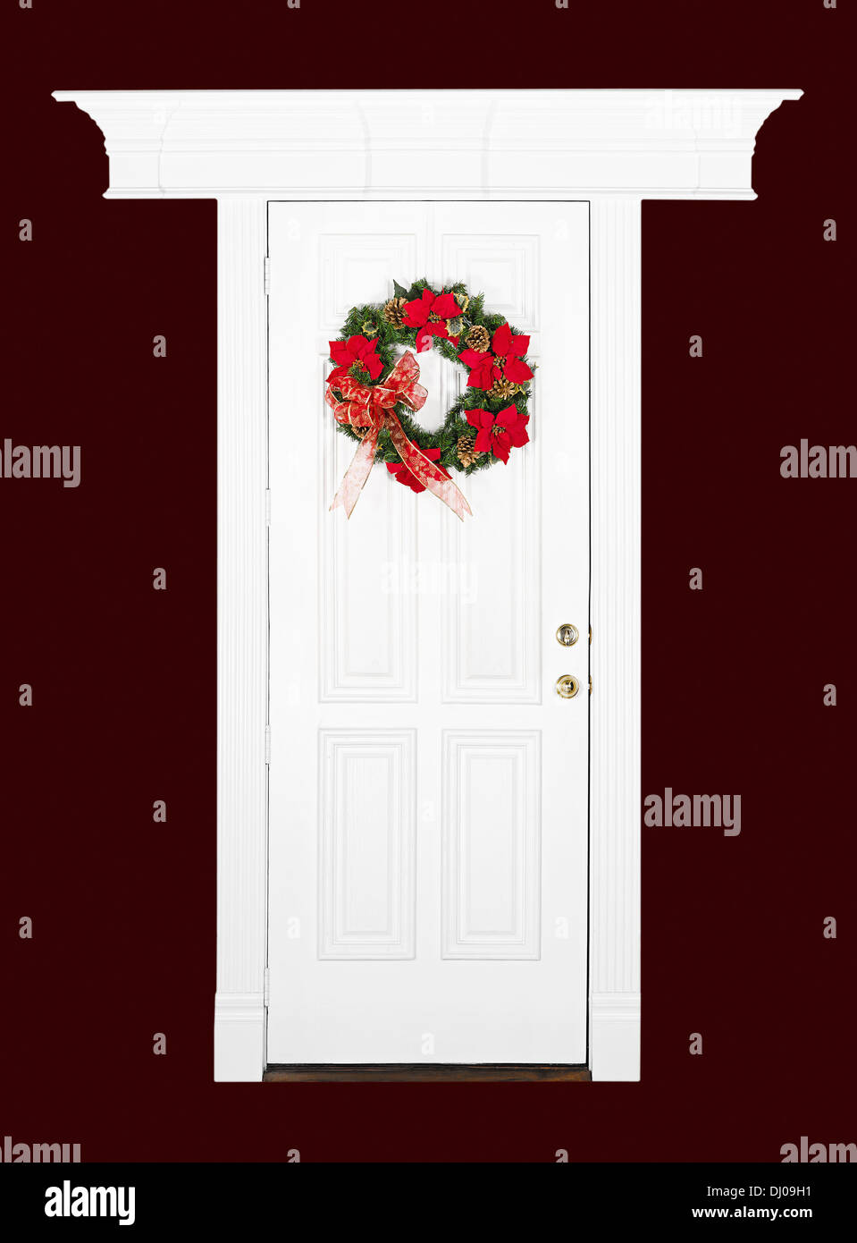 Fiore di Natale corona appeso sul bianco porta in legno con cornice decorativa, isolate su rosso scuro Foto Stock