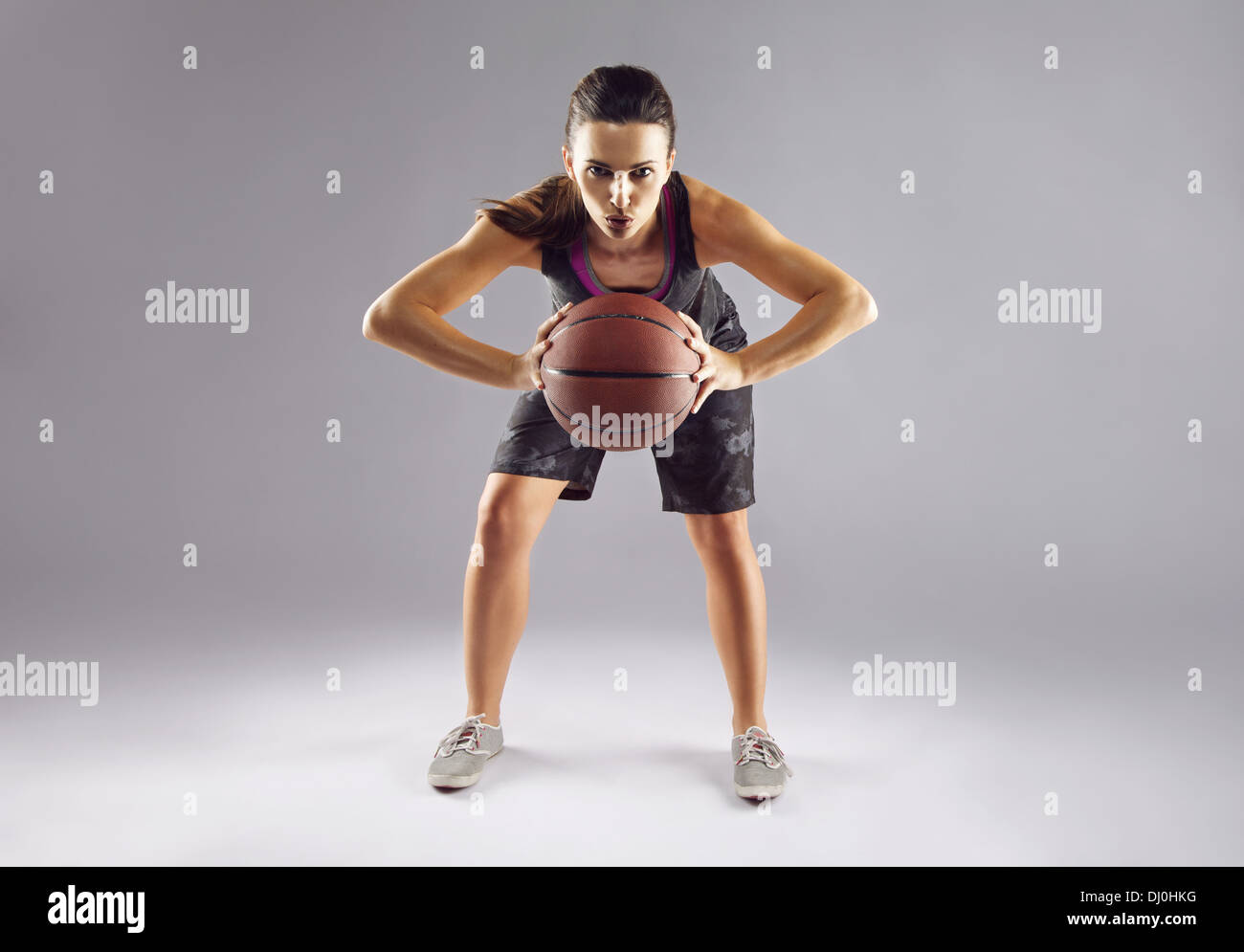 A piena lunghezza ritratto femminile di giocatore di basket passando la palla su sfondo grigio. Bellissima femmina in sportswear Foto Stock