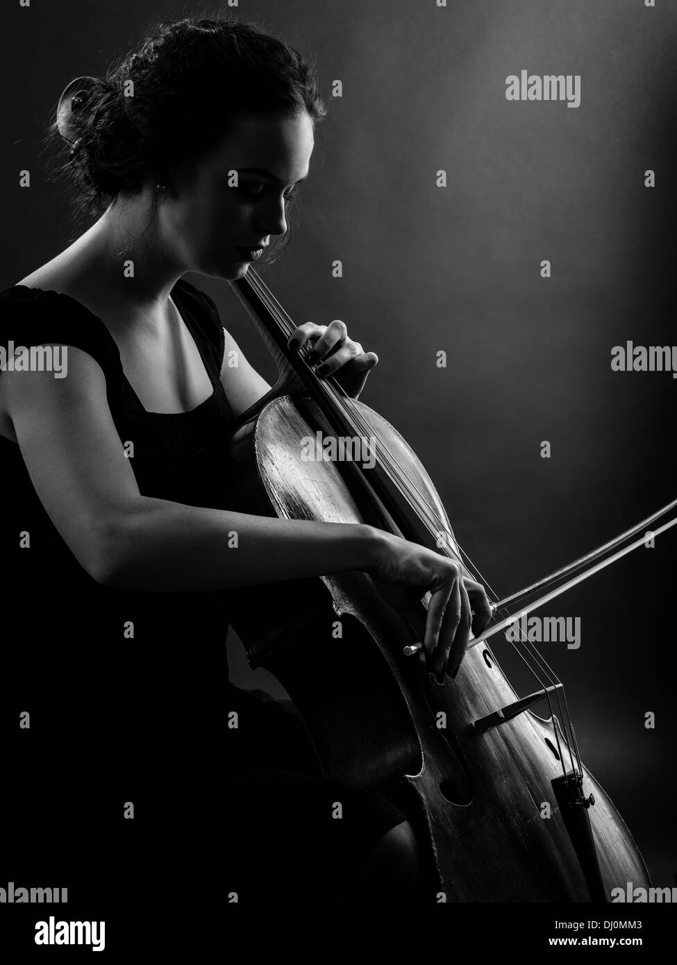 Foto di una bellissima femmina musicista giocando un violoncello. Backlit immagine in bianco e nero. Foto Stock