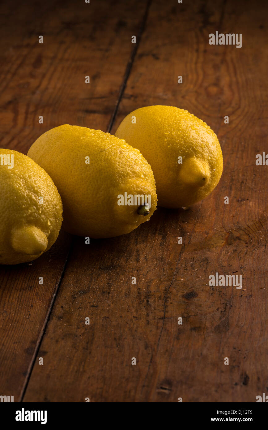 Tre limoni freschi allineati in una vita ancora disposizione con illuminazione calda sul vecchio tavolo in legno Foto Stock