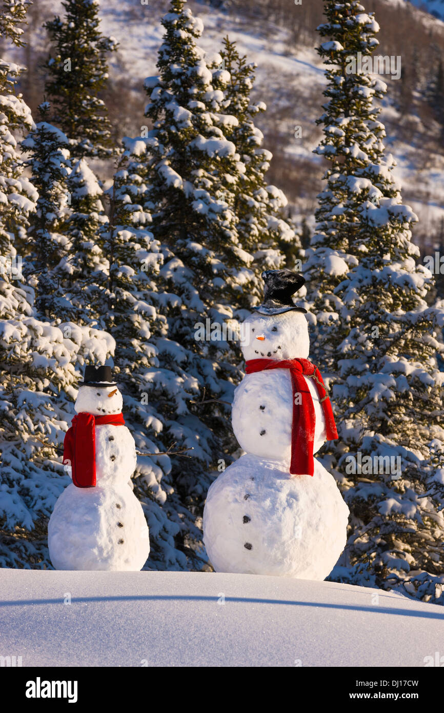 Due pupazzi di neve che indossa foulard rosso e Top cappelli in piedi di fronte a un abete Snowcovered Forest;Anchorage in Alaska Stati Uniti d'America Foto Stock