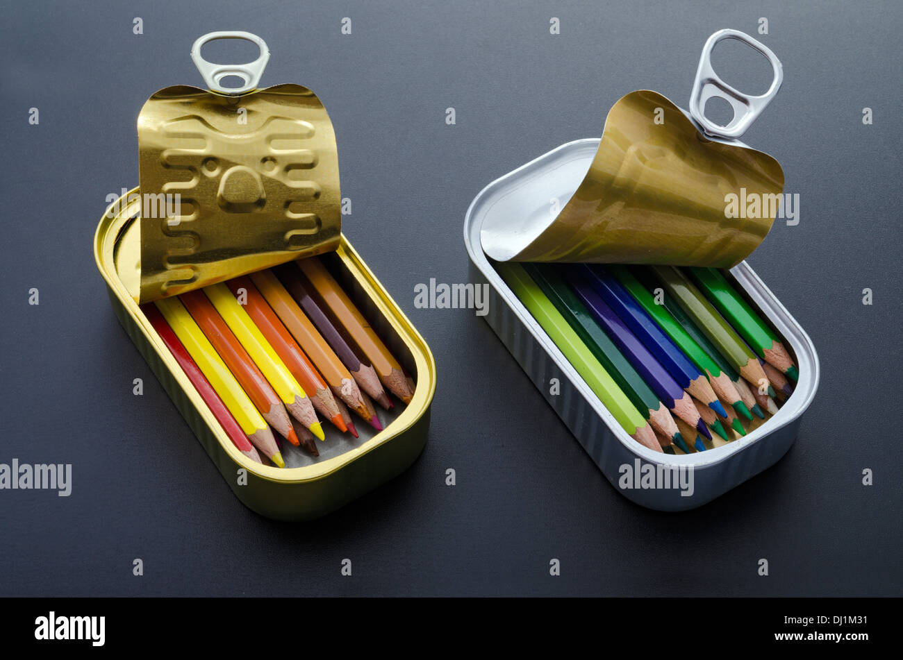 La disposizione delle due scatole di sardine riempita con ben ordinati matite colorate su sfondo nero. Foto Stock