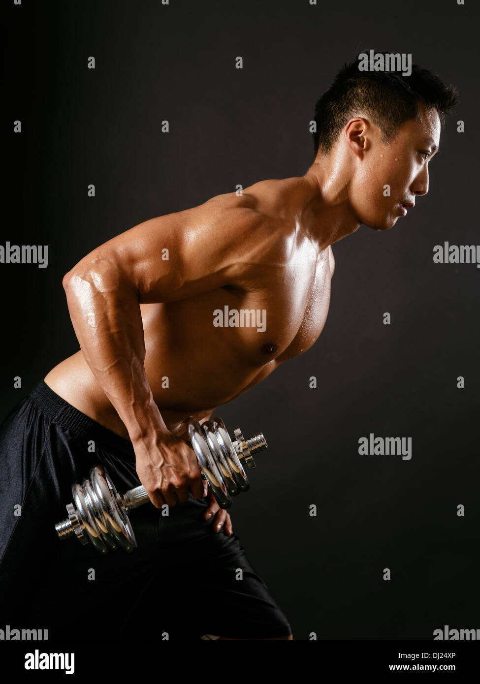 Foto di un maschio asiatici esercizio con manubri e il suo lavoro di tricipiti su sfondo scuro. Focus è sul braccio. Foto Stock