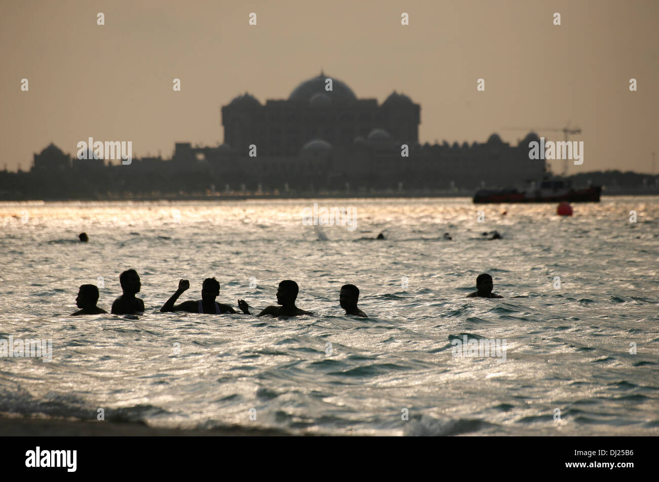 La popolazione locale e gli operai di nuotare in mare al largo della Corniche di Abu Dhabi con la Emirates Palace hotel in background Foto Stock