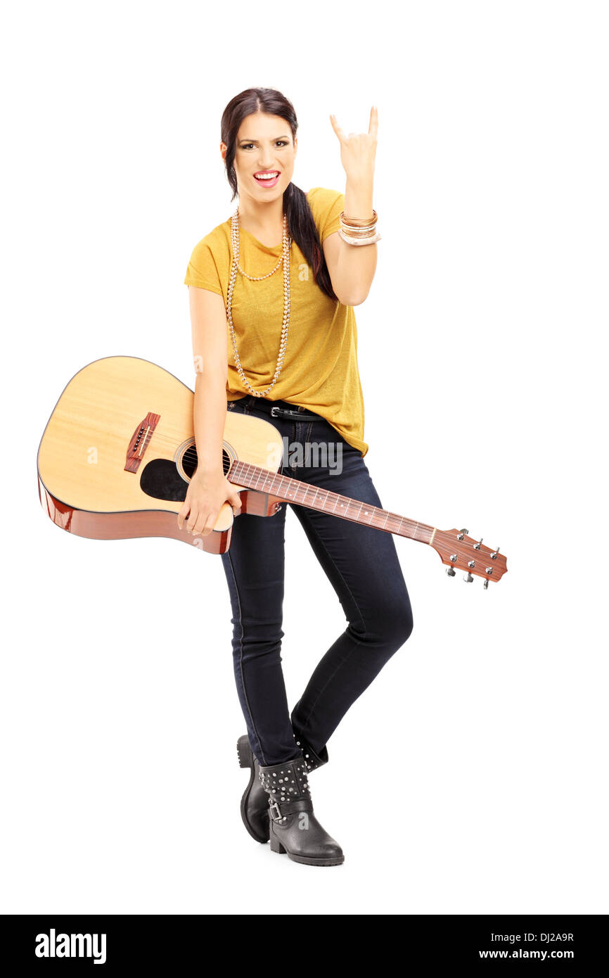 A piena lunghezza Ritratto di una giovane donna in possesso di una chitarra acustica e dando un rock and roll segno Foto Stock