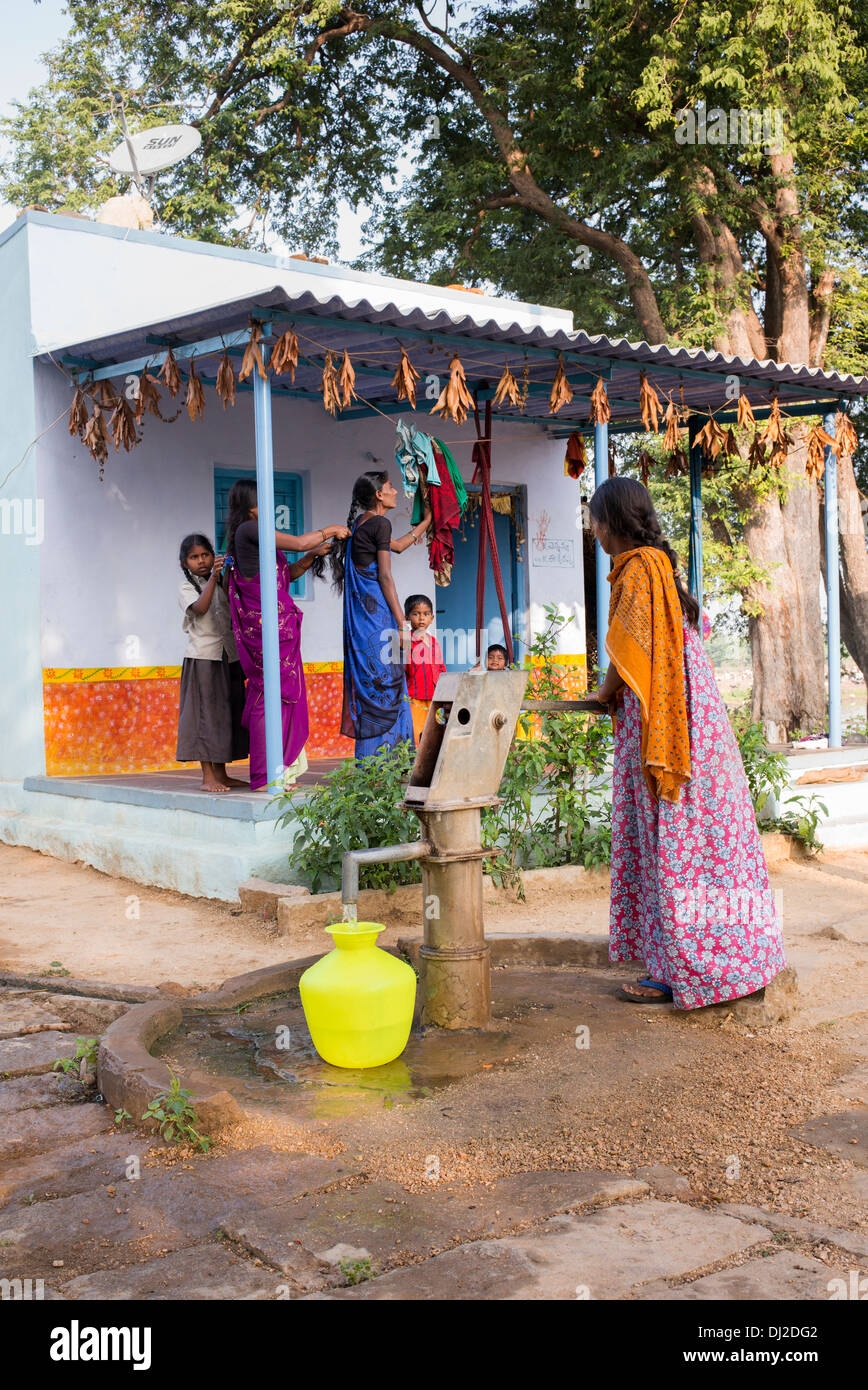 Donna indiana di riempimento acqua in plastica vaso da un villaggio rurale la pompa a mano. Andhra Pradesh, India Foto Stock