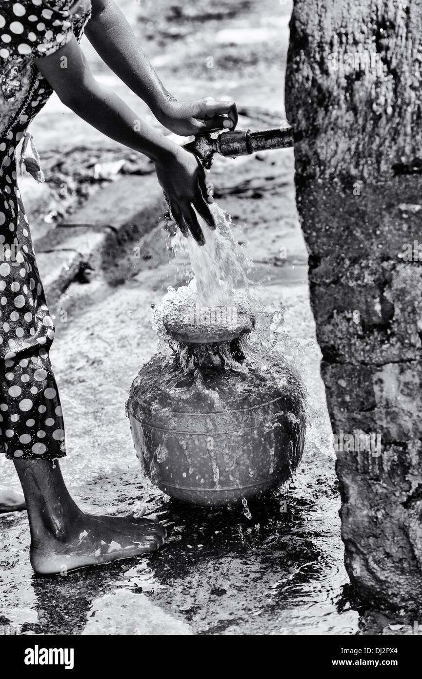 Ragazza indiana il riempimento di un contenitore di plastica con acqua da un tubo montante in un territorio rurale villaggio indiano. Andhra Pradesh, India. In bianco e nero. Foto Stock