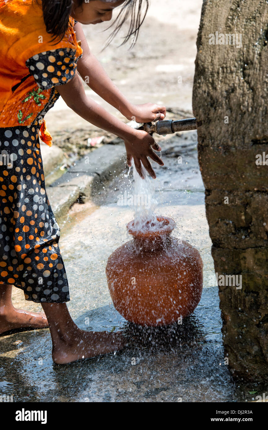 Ragazza indiana che porta un vaso in materia plastica con acqua da un tubo montante in un territorio rurale villaggio indiano street. Andhra Pradesh, India Foto Stock