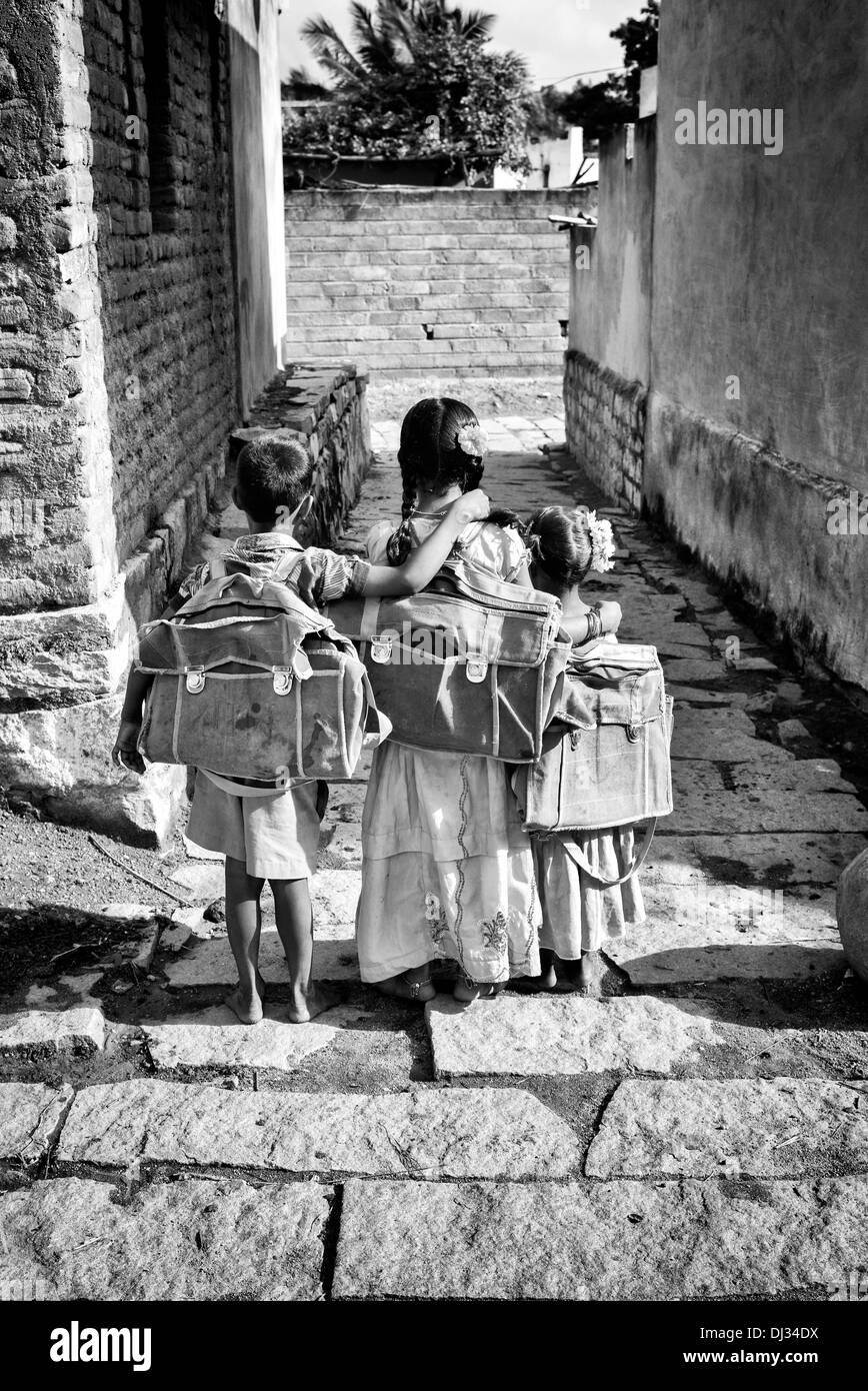 Tre piccoli bambini indiani andando a scuola in un territorio rurale villaggio indiano. Andhra Pradesh, India. Monocromatico Foto Stock