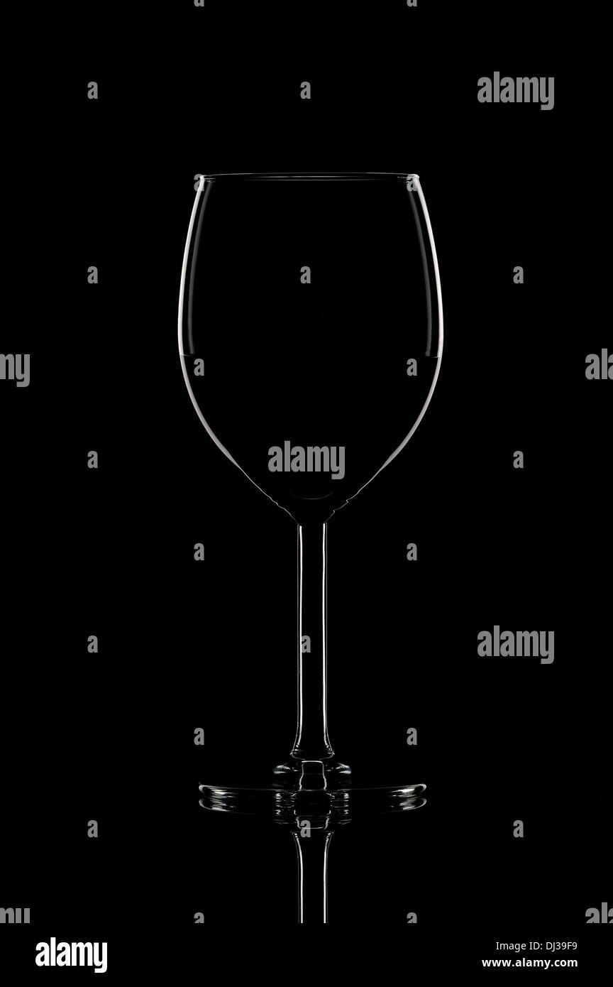 Un vino elegante bicchiere con vino rosso brillare su sfondo nero con la riflessione. Luce di contorno. Foto Stock