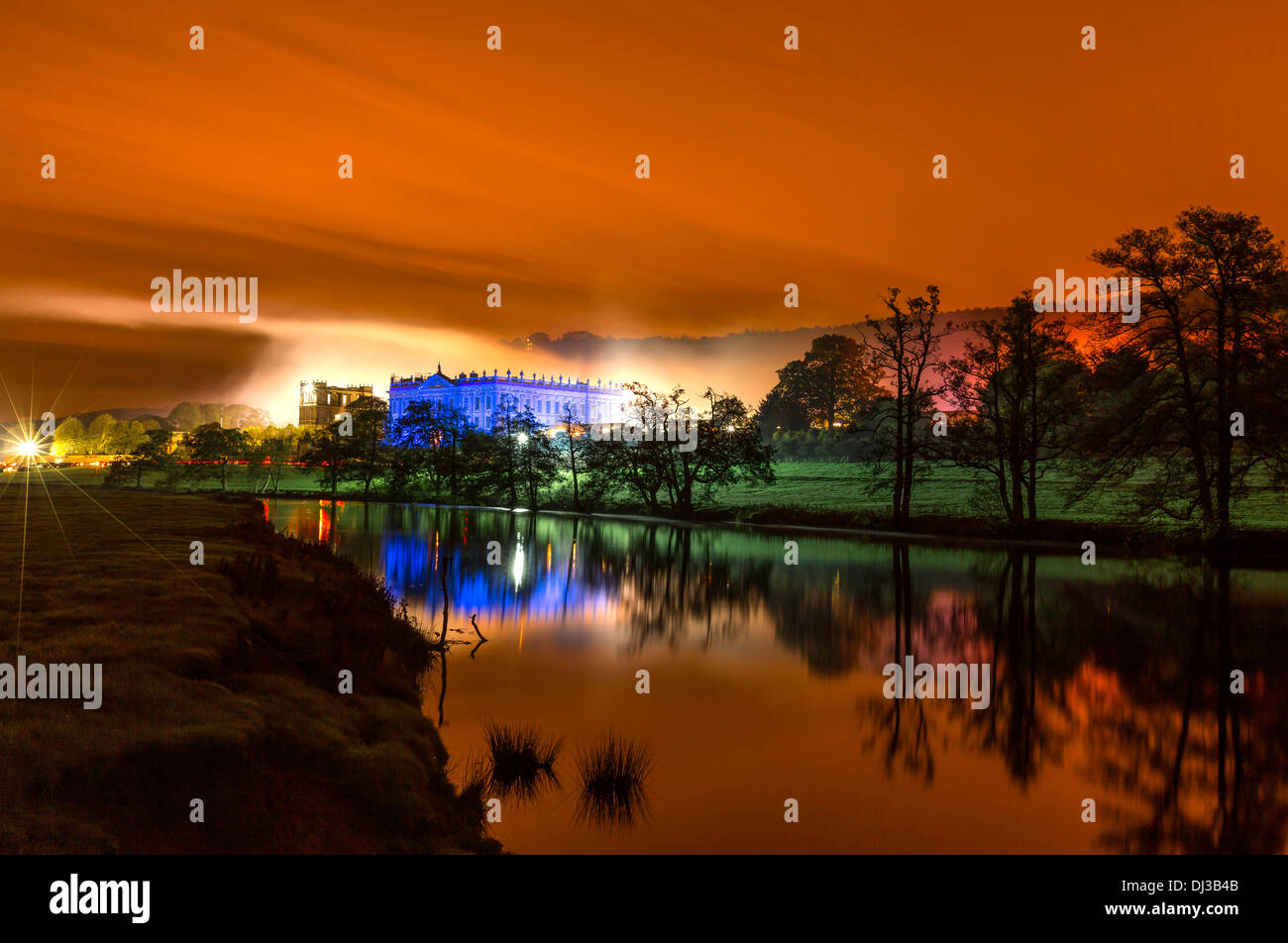 Chatsworth House di notte prese attraverso il fiume Derwent subito dopo una di fuochi d'artificio e falò, con un luminoso cielo arancione. Foto Stock