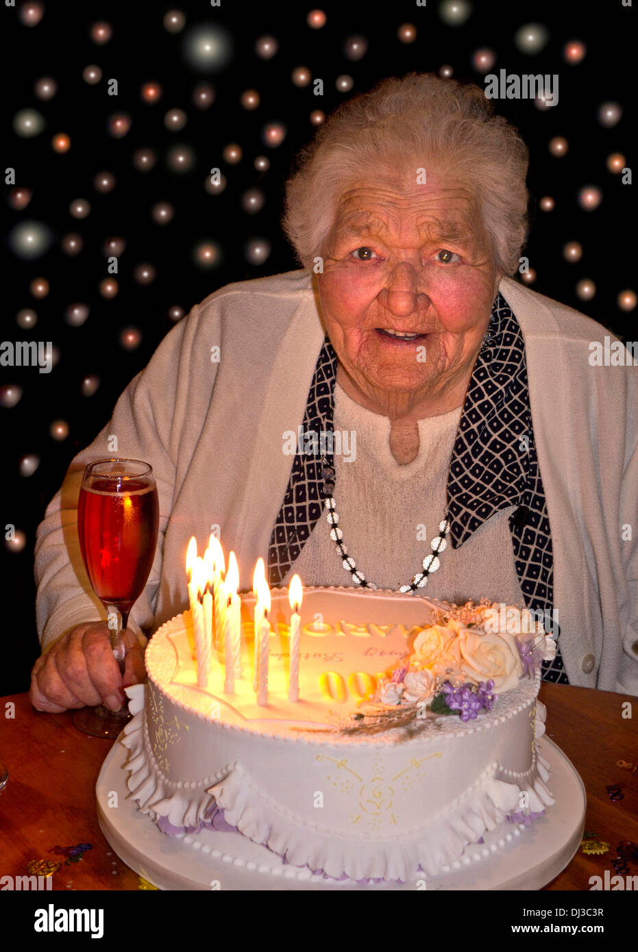 Celebrazioni di 100 anni Felice allerta donna anziana a 100 anni di età con la sua torta di compleanno e un bicchiere di champagne rosa. 100 luci sullo sfondo Foto Stock