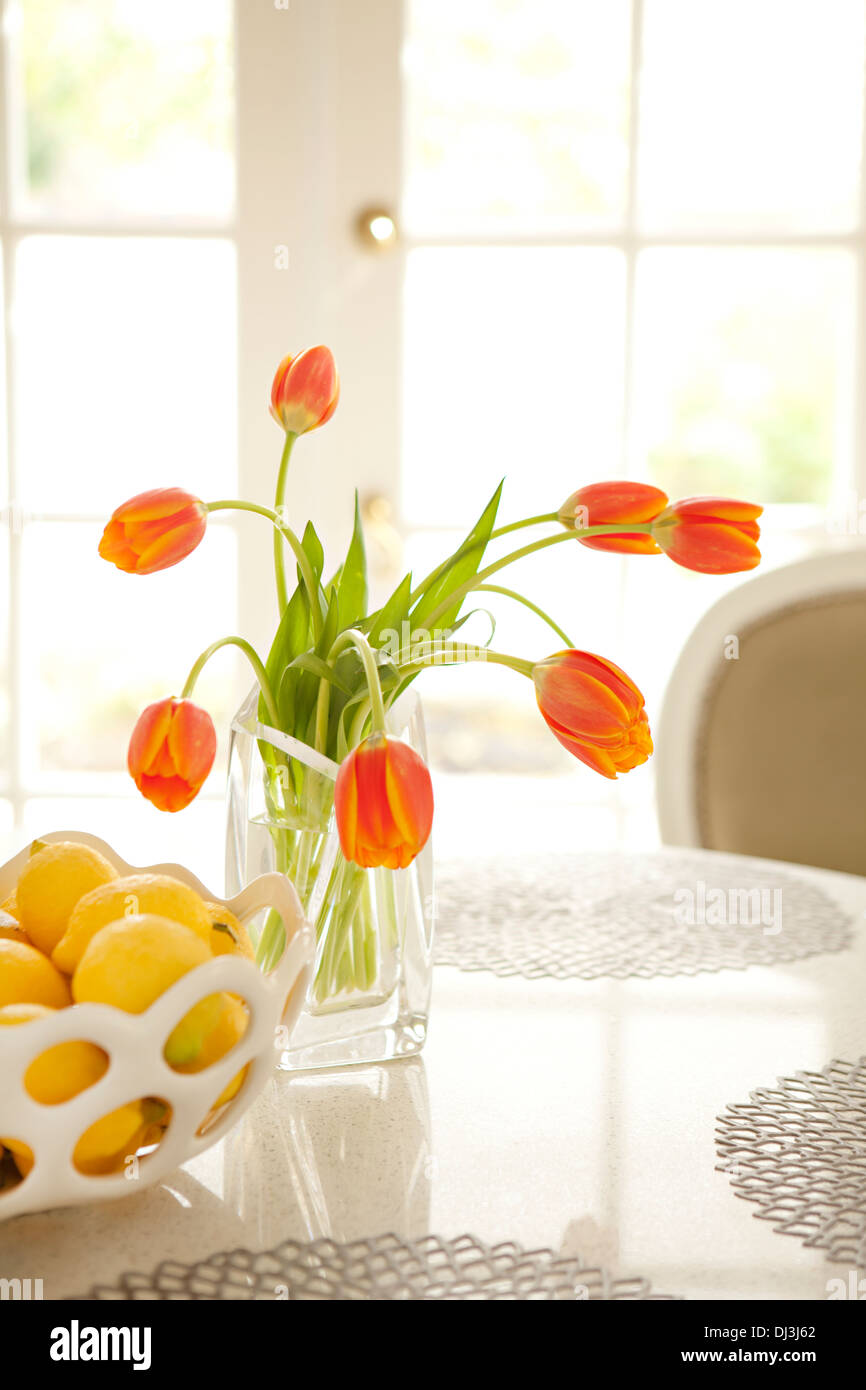 Tulipani arancio e limoni su tavola nella soleggiata sala da pranzo Foto Stock