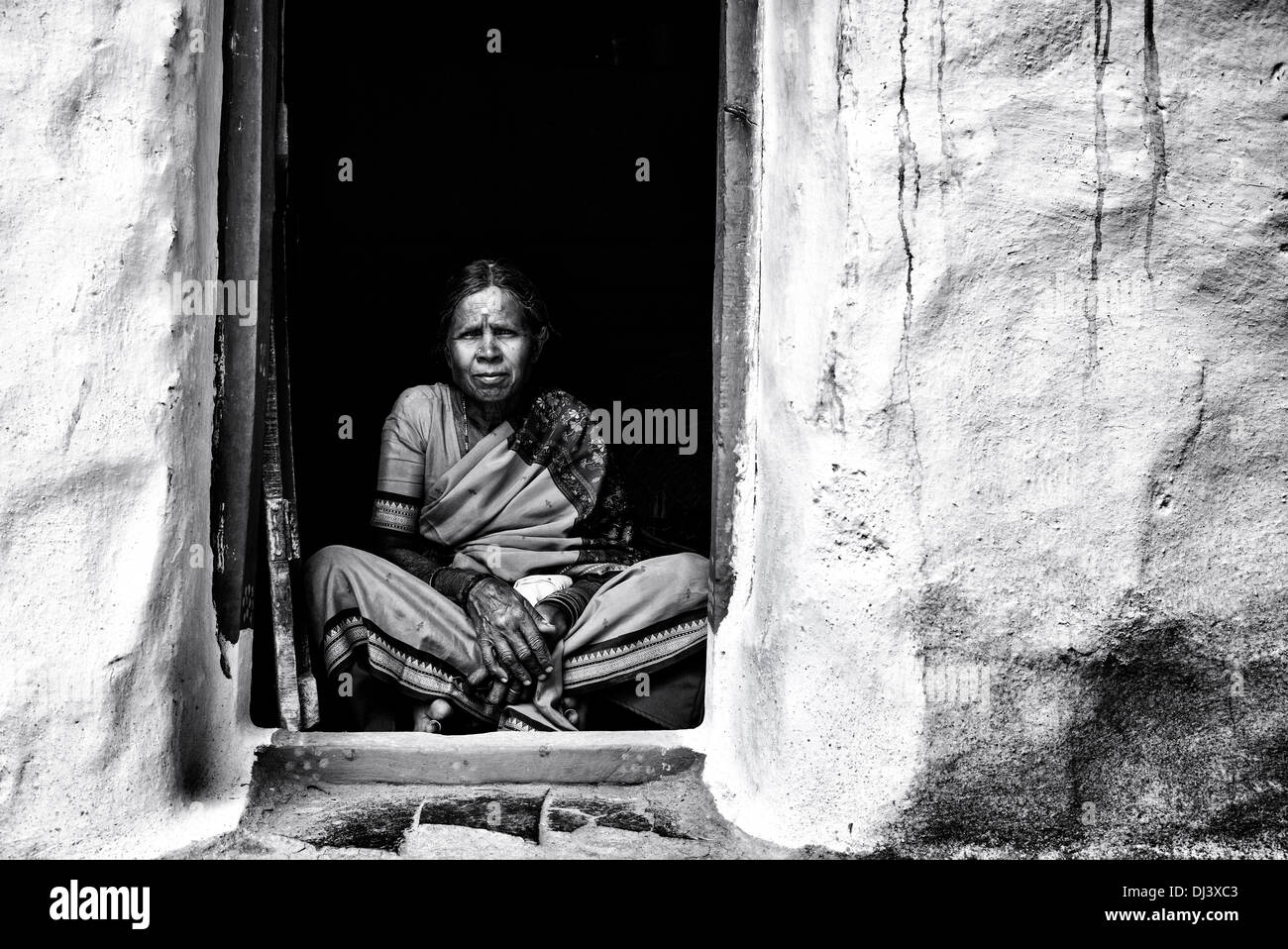 Anziani donna indiana seduto nel suo porta del suo villaggio rurale home. Andhra Pradesh, India. In bianco e nero. Foto Stock