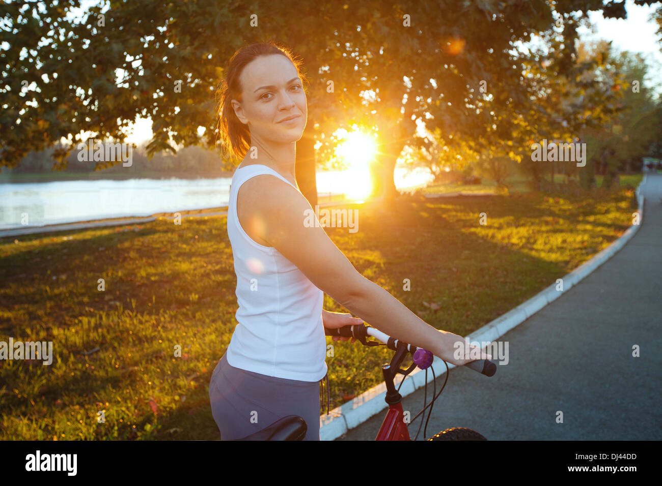 Giovane donna sorridente con la bicicletta nel parco Foto Stock
