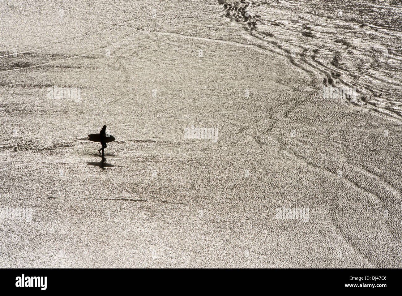 Stagliano surfers mostrato contro quasi un riflesso metallico di luce sull'acqua a Saunton sands beach, Devon, Regno Unito Foto Stock