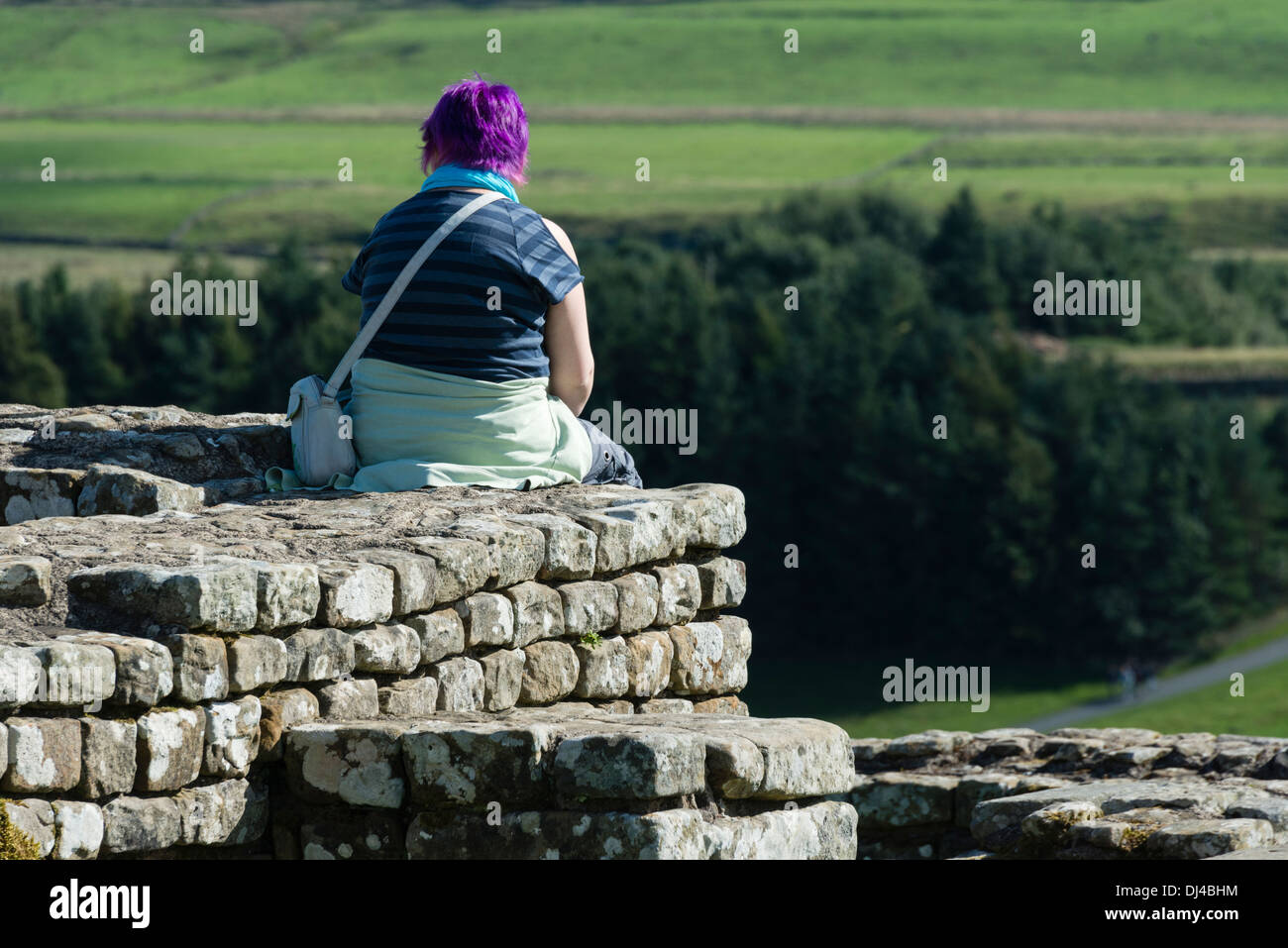 Ragazza seduta sulla parete in corrispondenza di Housesteads Roman Fort Foto Stock