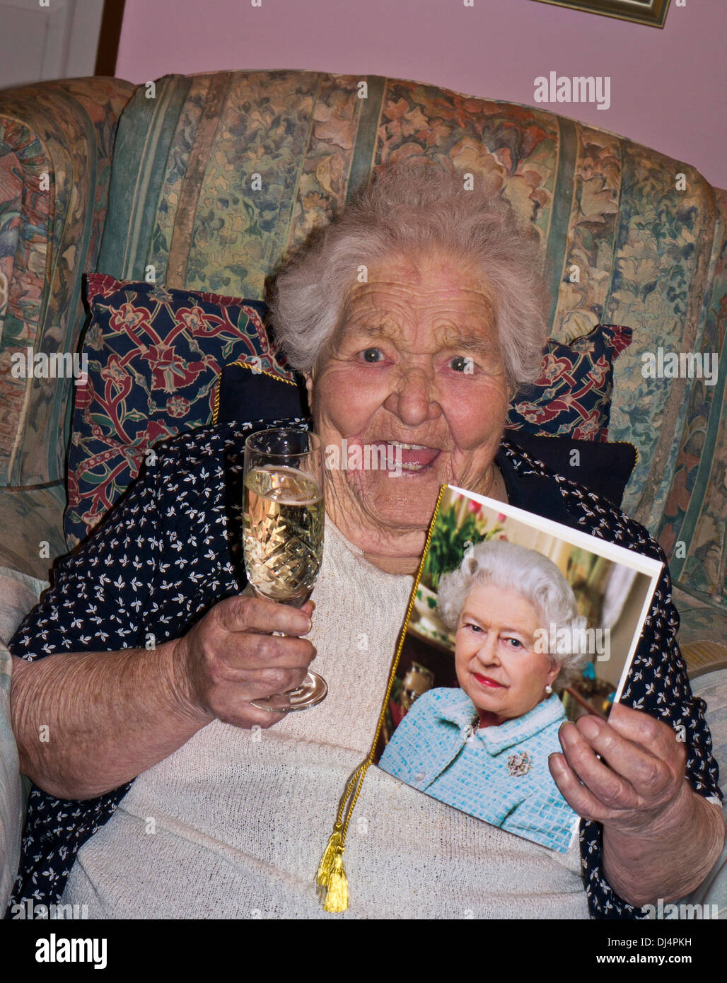100 anni. Felice allerta donna anziana vitale a 100 anni con un bicchiere di champagne e la tradizionale tessera di congratulazioni di HM la Regina Foto Stock