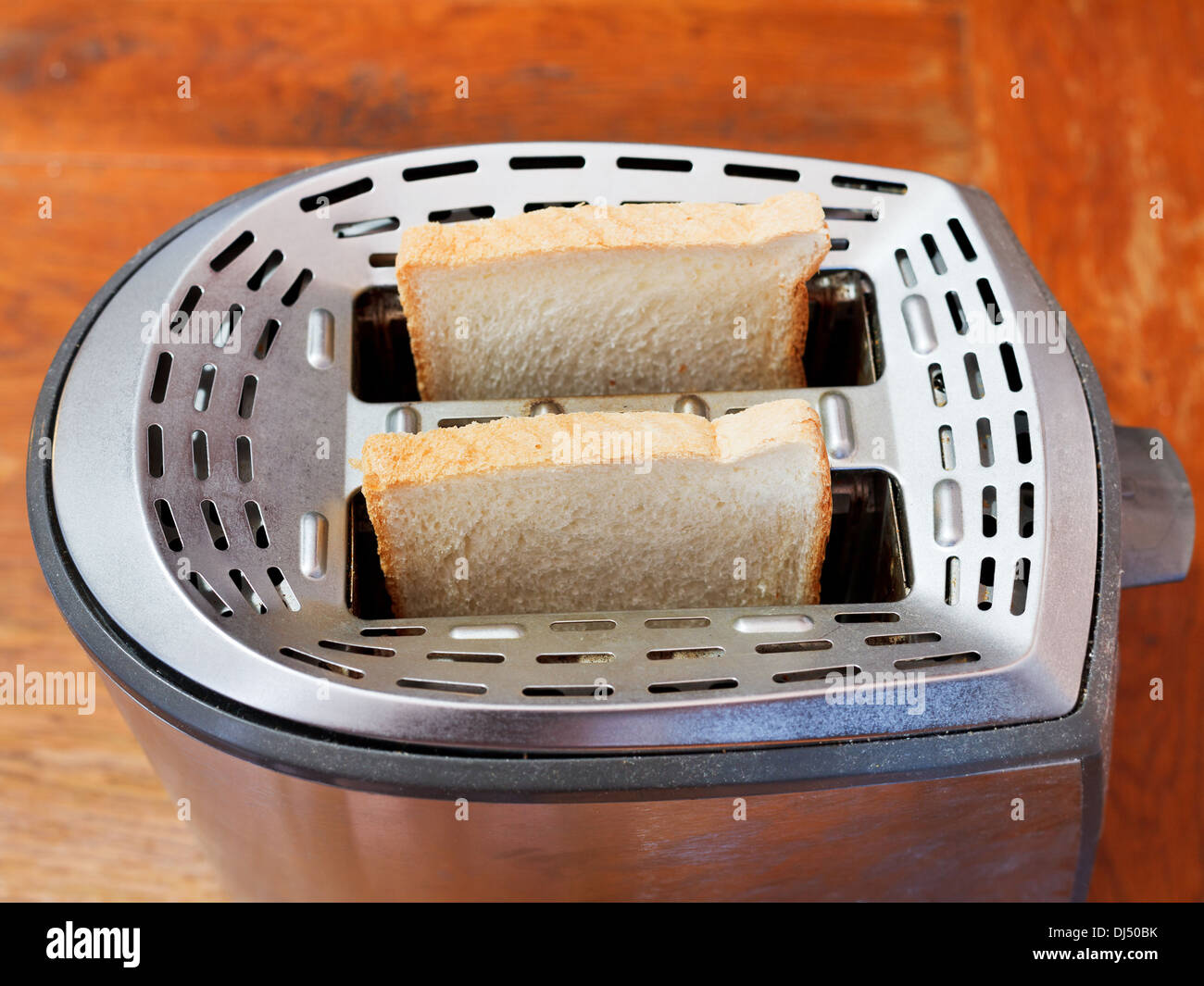 Due nuove fette di pane nel tostapane metallico sul tavolo di legno Foto Stock