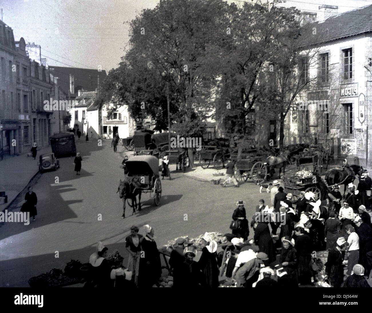 Foto storica del 1930s che mostra una strada a Liegi, Belgio, con la gente del posto che frequenta un mercato di abbigliamento all'aperto. Un cavallo & cart va giù per la strada. Foto Stock