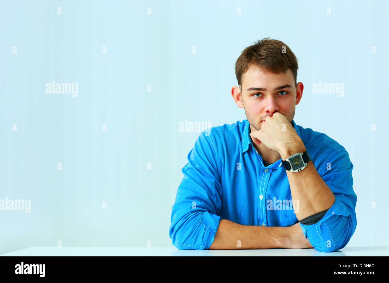 Ritratto di un giovane imprenditore pensieroso in maglietta blu in ufficio Foto Stock