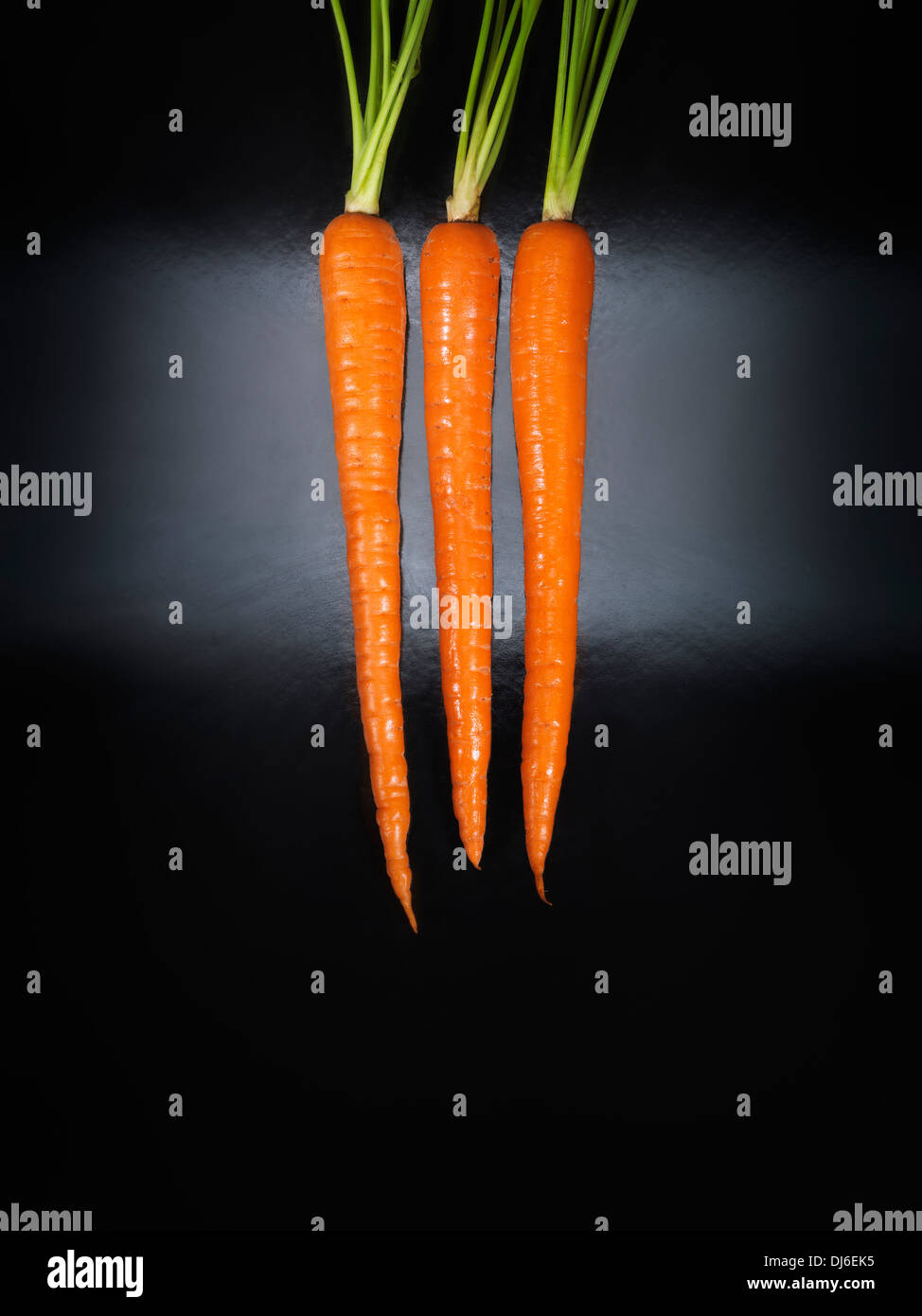 Artistico cibo concettuale ancora la vita di tre carote arancione isolati su sfondo nero Foto Stock
