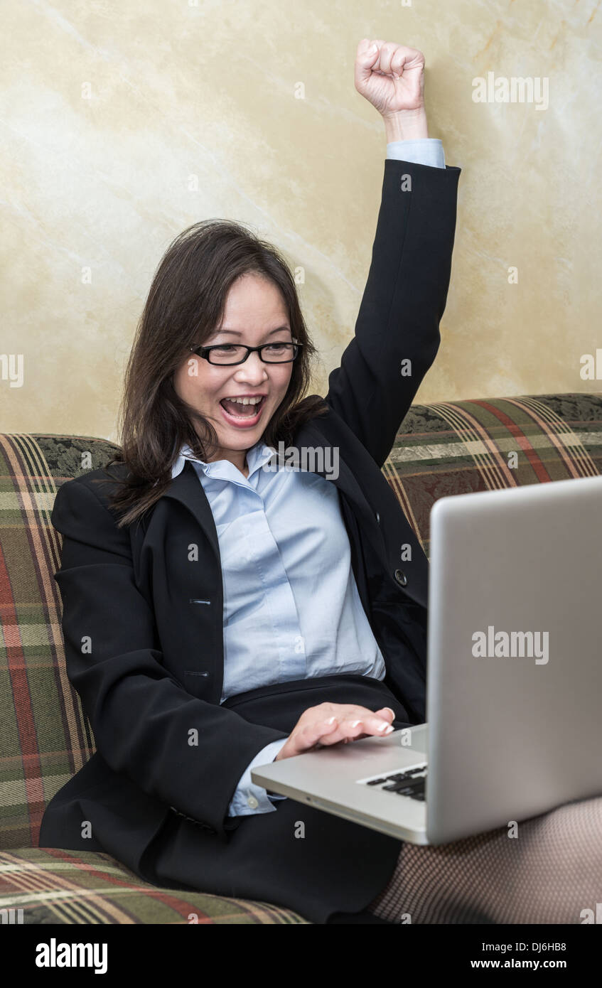 Professional woman in business suit sul divano il tifo con i pugni in aria con il computer portatile Foto Stock