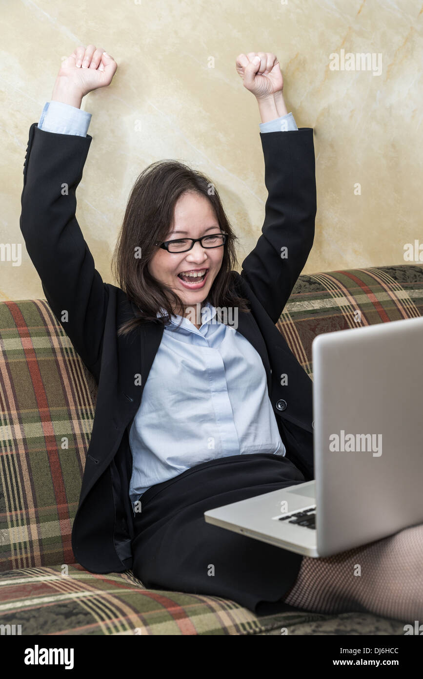Professional woman in business suit sul divano il tifo con i pugni in aria con il computer portatile Foto Stock