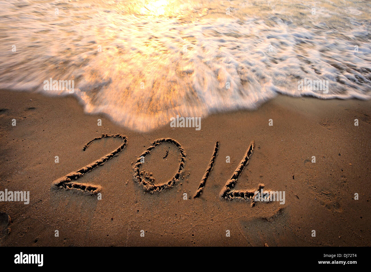 Anno Nuovo 2014 inciso sulla spiaggia inviare con onde, al tramonto del tempo. Foto Stock