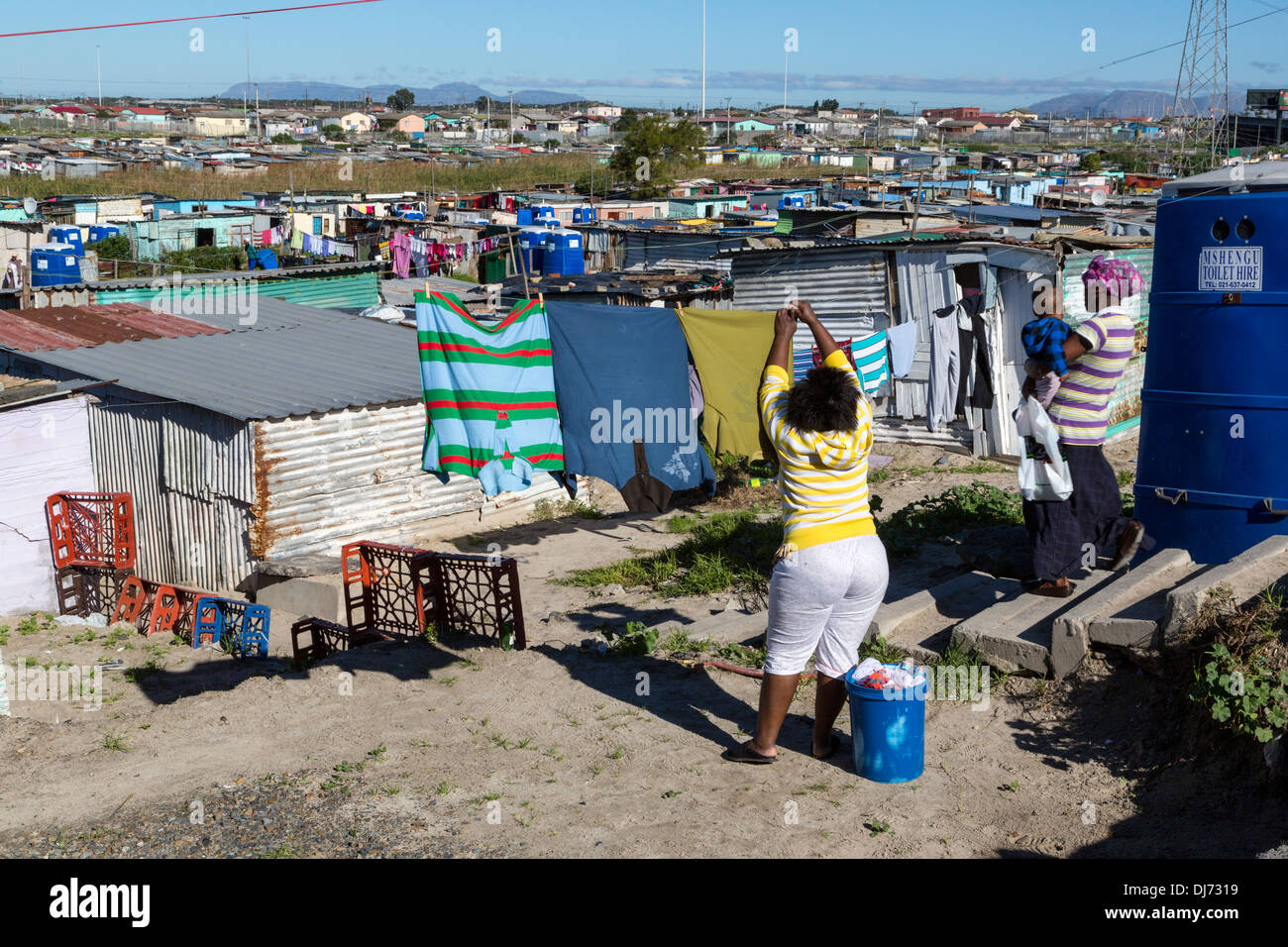 Sud Africa, Cape Town, Khayelitsha Township. Donna appeso il suo servizio lavanderia. Nota il blu outdoor bagni portatili. Foto Stock