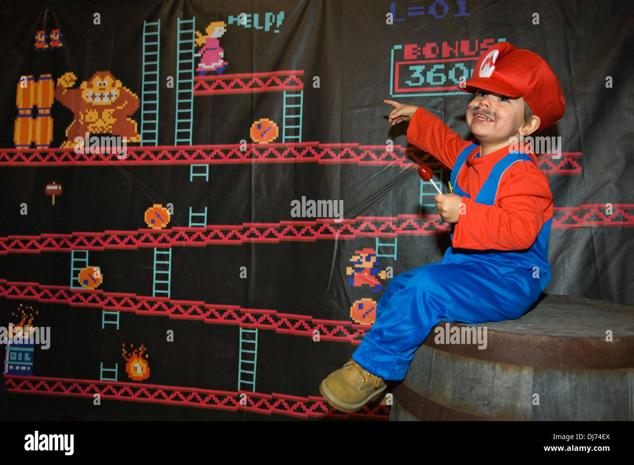 Bambino vestito come Mario seduto sulla canna con Donkey Kong Banner dietro al lo Zoo di Louisville festa di Halloween a Louisville Foto Stock
