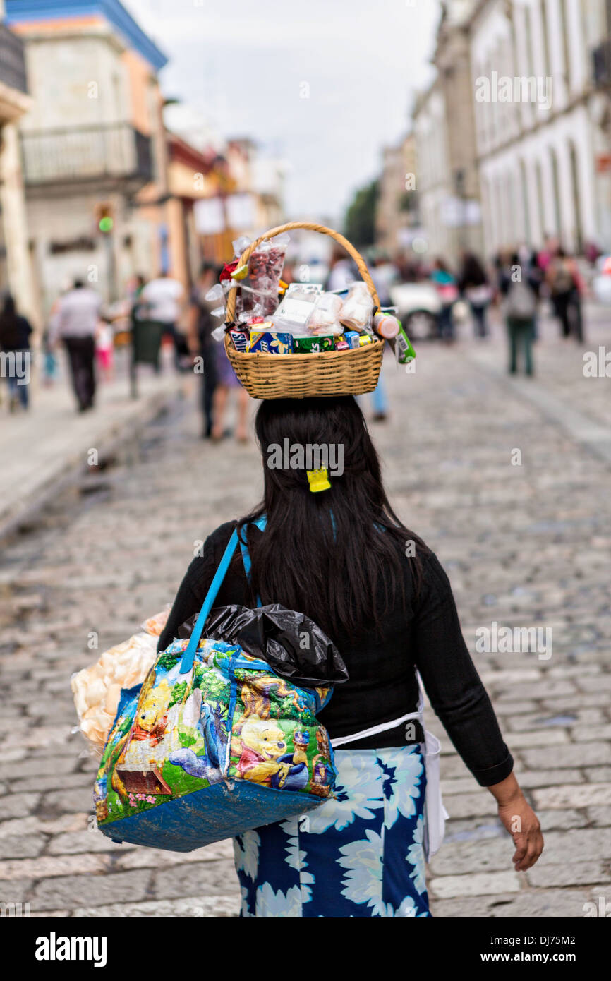 Un messicano venditore ambulante cammina per il Alcala pedonale con la sua merce equilibrato sul suo capo a Oaxaca, Messico. Foto Stock