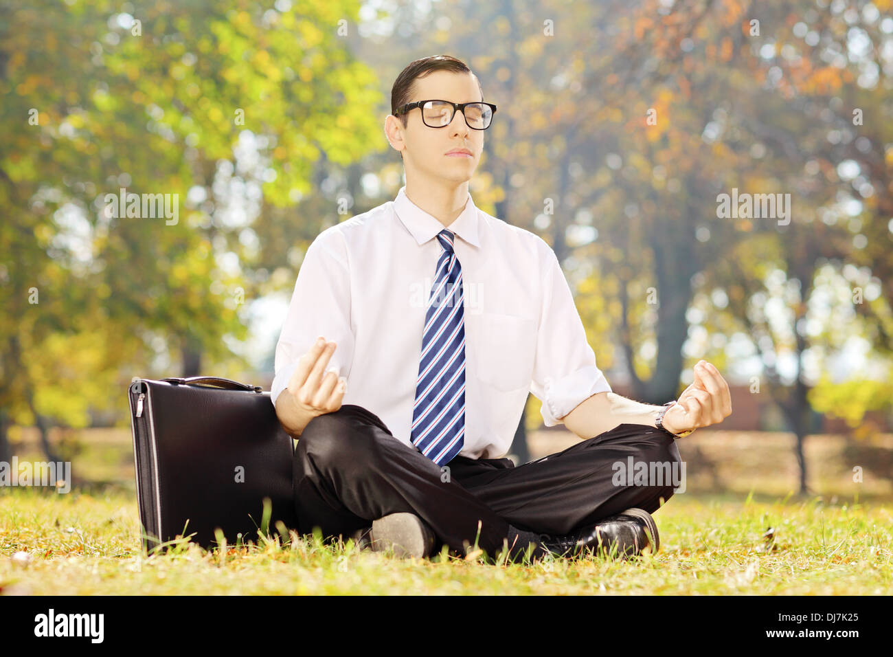 Imprenditore giovane seduto su un prato verde meditando in un parco Foto Stock