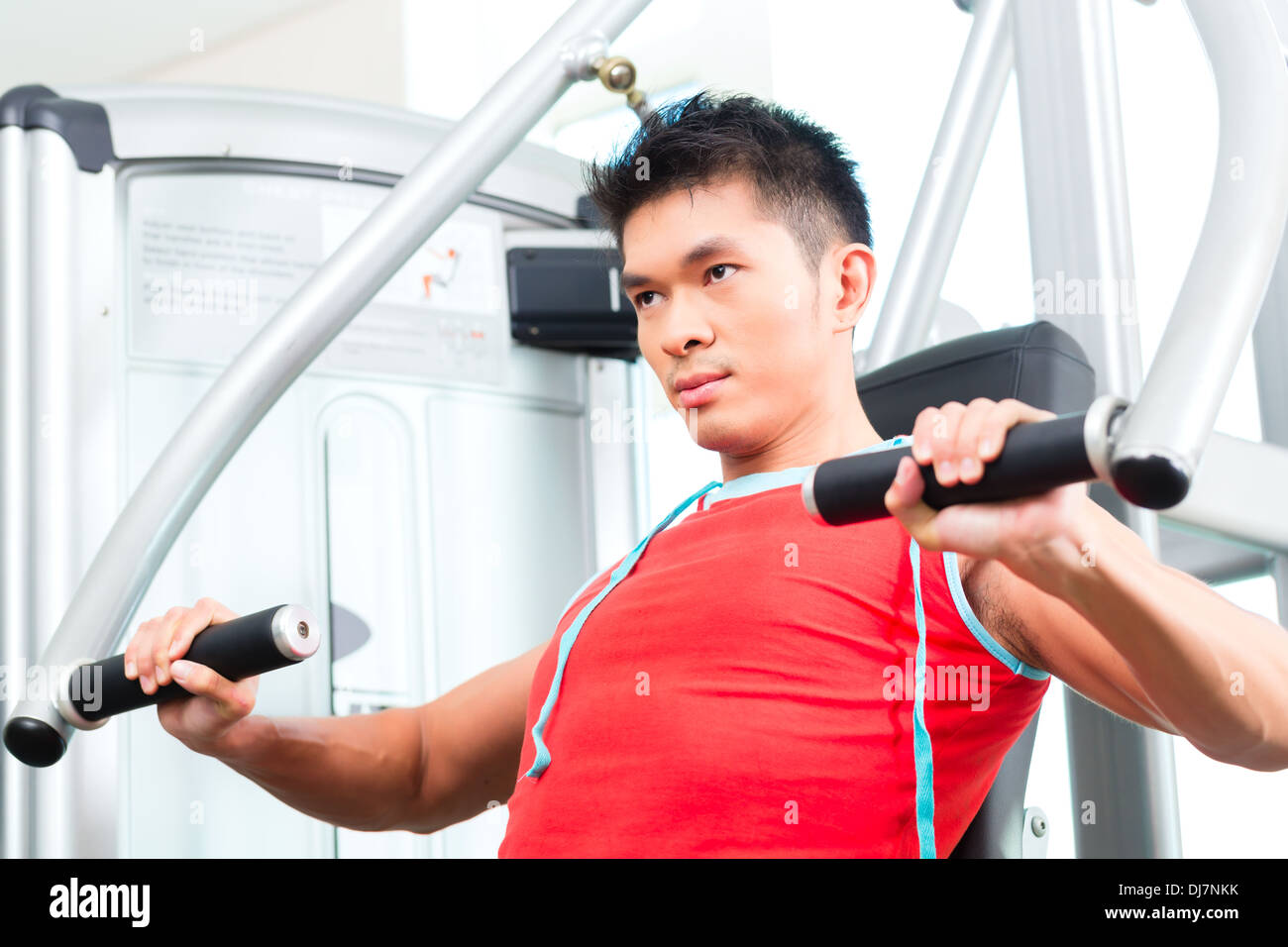 Asian uomo cinese avente fitness training o allenamento in palestra facendo sport per costruire muscolo su una macchina di peso Foto Stock